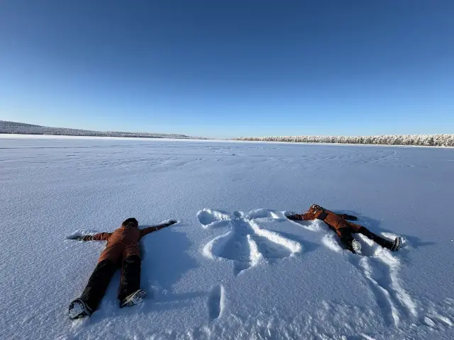 Children in their included Arctic snowsuits making snow angels in Lapland