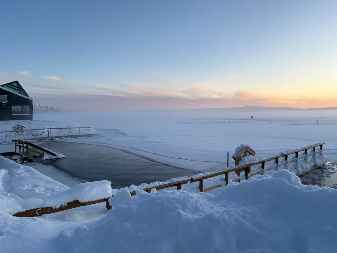 Arctic Sauna World beside a snow-covered lake at sunset